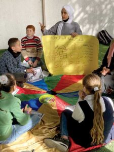 Young woman in a headscarf holing a drawn image in front of schoolchildren